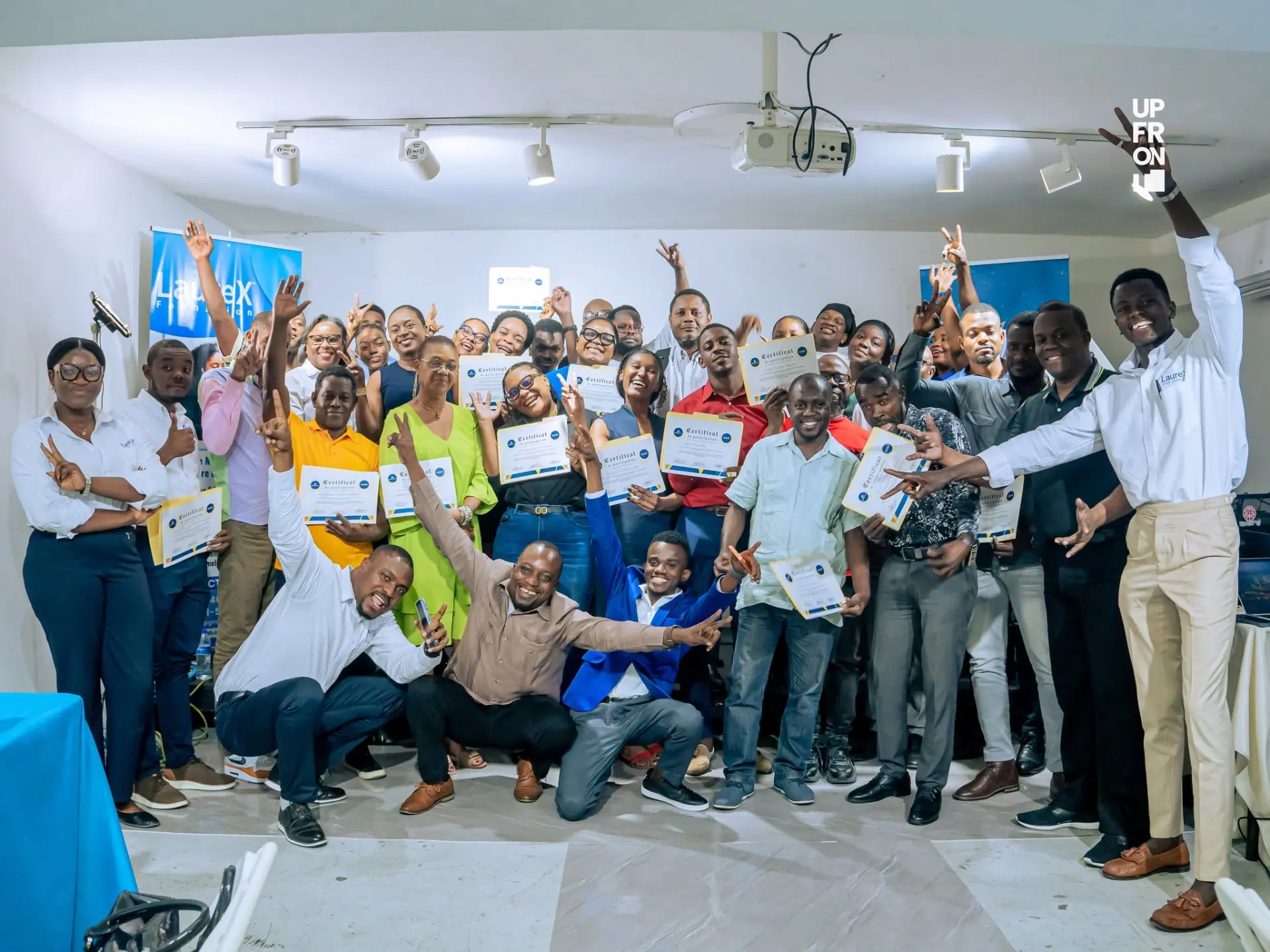 Groupe de participants tenant leurs certificats de participation et levant les bras devant un kakemono LaureX Formation